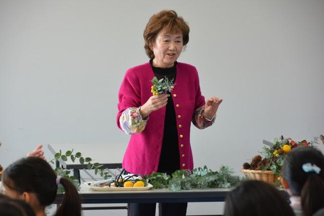 講師の女性が植物を手に持ち、話している写真