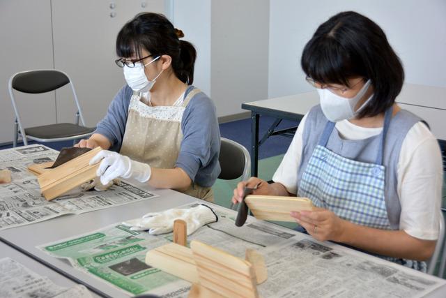 参加者の女性が紙やすりで磨き、木の角を丸くしている写真