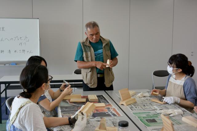 参加者を前に、講師である北杜市で木工教室を主宰する清水三郎さんが説明をしている写真