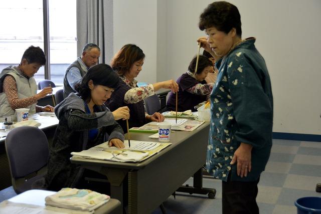 筆を持って取り組んでいる参加者の前に立つ講師の清水さんの写真