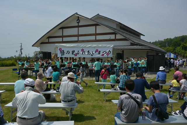 屋外ステージで敷島吹奏楽団によるミニコンサートが開かれている写真