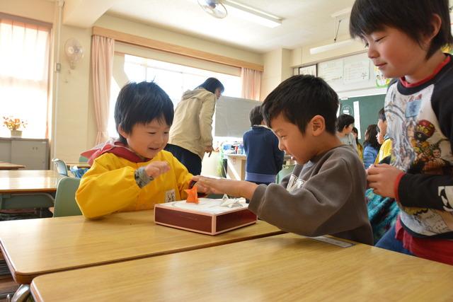 楽しそうに紙相撲で遊ぶ児童と園児の写真