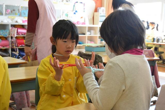 あやとりで遊ぶ児童と園児の写真