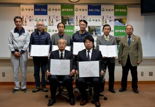 (写真)調印した協定書を披露する株式会社中村建設の関係者、各自治会区長、甲斐市長