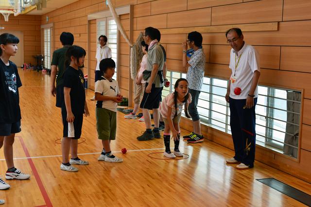 女の子が体育館で赤いまるの中に立ち赤いボールを投げている写真