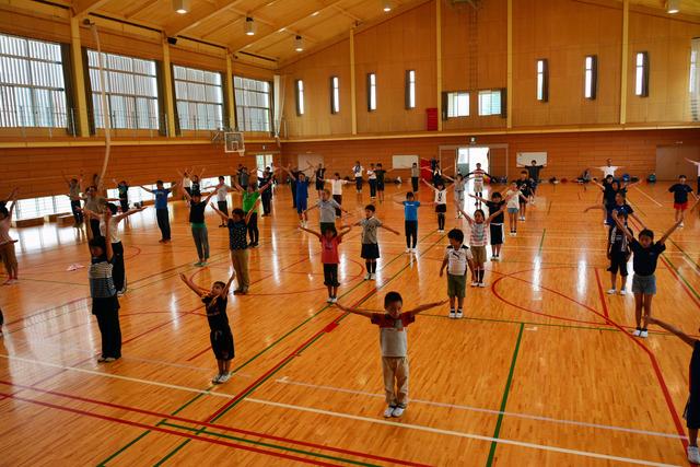 体育館で大人も子どもも並んでラジオ体操を行っている写真
