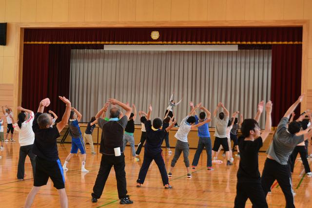 体育館で大人も子どもも並んでラジオ体操を行っている写真