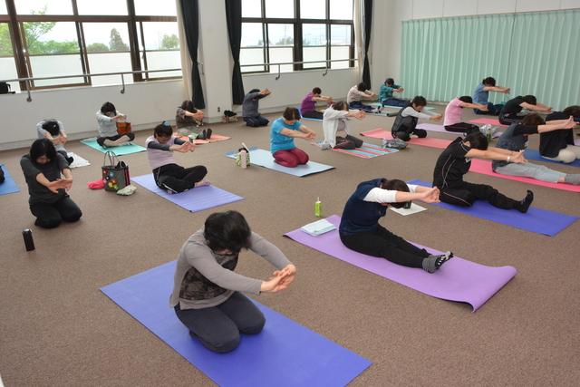 足を延ばして座り組んだ手を体の前に伸ばし、整体体操を行う参加者たちの写真