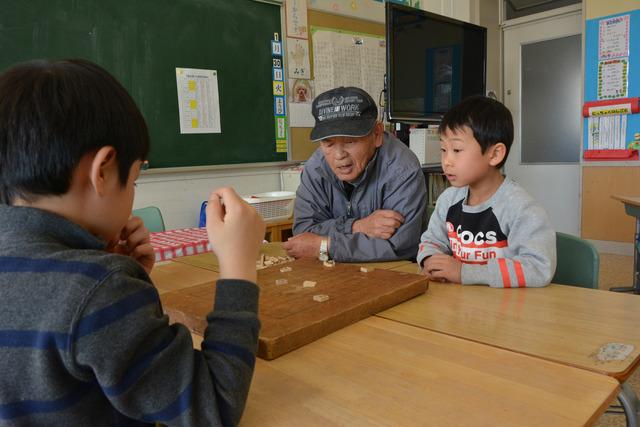 教室で、先生と将棋をする児童たちの写真