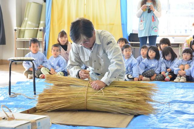 大き目の缶の周りに配置した藁を縄で縛っている小澤さんの写真