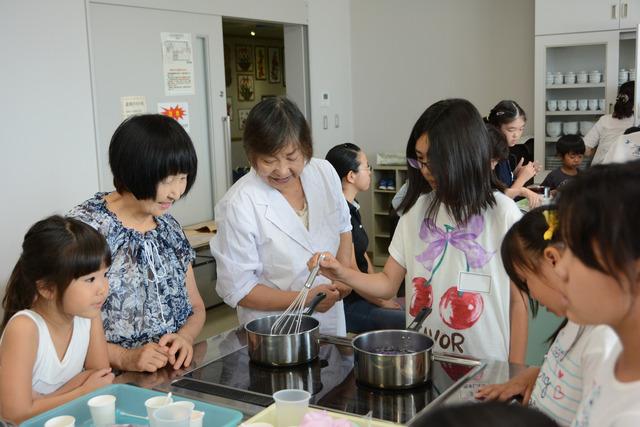 講座「キッチンで科学しよう」にてムラサキキャベツの煮汁を作る女子小学生とその様子を見つめる講師と保護者の写真