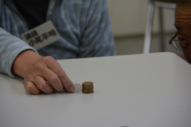 テーブルの上で10円硬貨を13枚積み重ね、1円硬貨の高さと比べている様子の写真