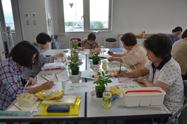 鉢植えの花を見ながら絵を描く人々の写真