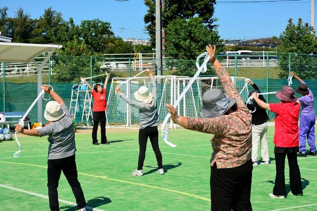 島上条公園で大勢のシニアの方が指導員のもと紐を使用してストレッチをしている写真