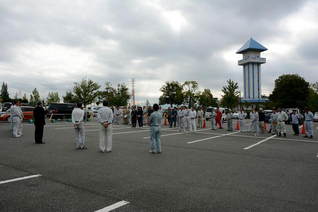 ドラゴンパーク駐車場で作業着を着た男性が集まり開始式を行っている写真
