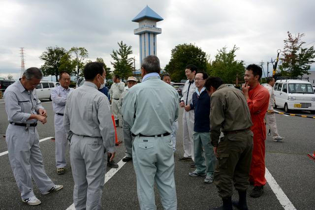 駐車場で作業着を着た複数の男性が話をしている写真