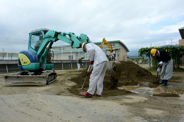 作業員が双葉東小学校駐車場の整地と砕石の敷きならしを重機や道具を使って行っている写真