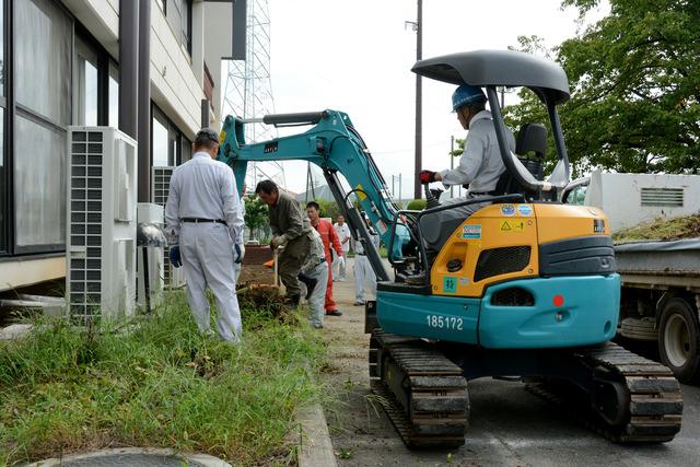 作業員が重機に乗って竜王南部公民館の花壇の除草や抜根などの作業を行っている写真