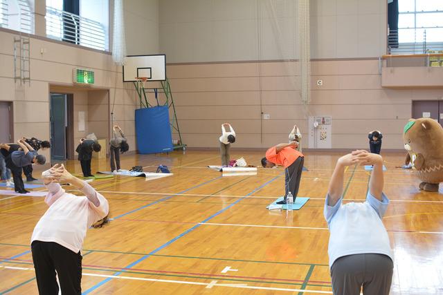 敷島体育館で先生を中心に参加者が円になって、手を組み背中の後ろに腕を伸ばしている写真