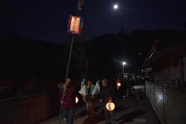 夜道を提灯と纏いを持った複数の男性が歩いている写真
