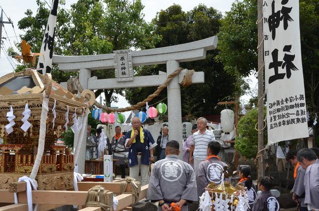 神社の鳥居の前に神輿が置かれ、鳥居の下で話をしている人の写真