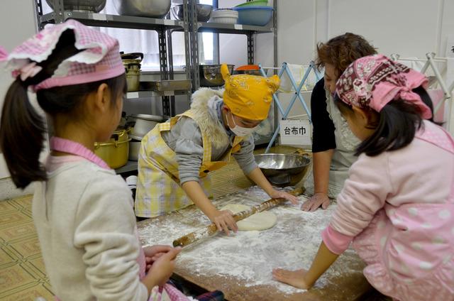 麺生地を棒で伸ばしている子どもの写真