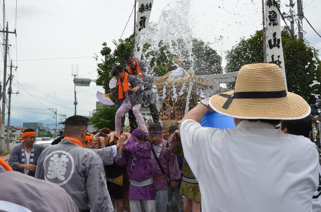 神輿を担いでいる人々に水がかけられている写真