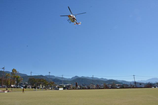 広い芝生の広場を低空で飛ぶヘリコプターの写真