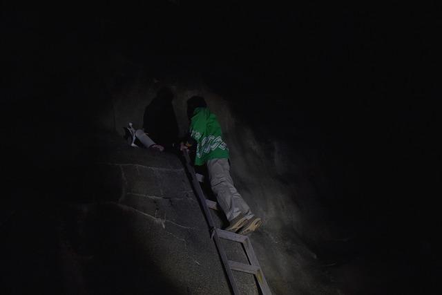 暗い中、緑の法被を着た男性が梯子を上っている写真