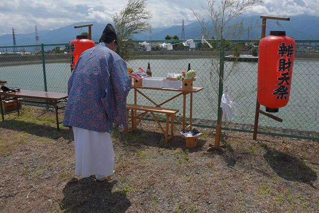 大溜池で神主が提灯やお供え物の前で今年の豊作と適量の雨を祈願している写真