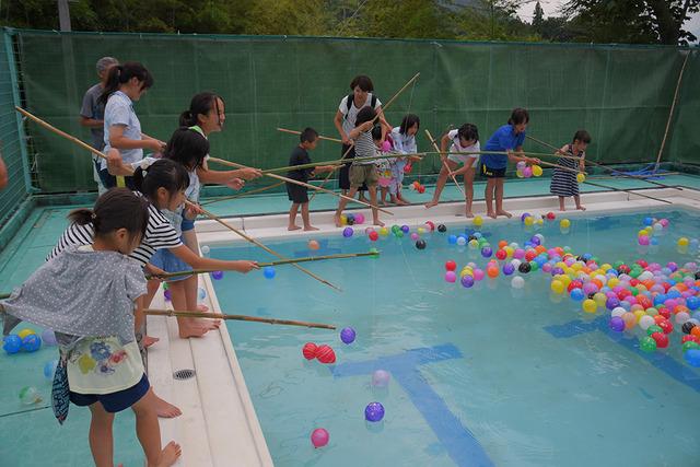 プールにたくさんのヨーヨーが浮かびそれを竹の竿で釣っている子ども達の写真