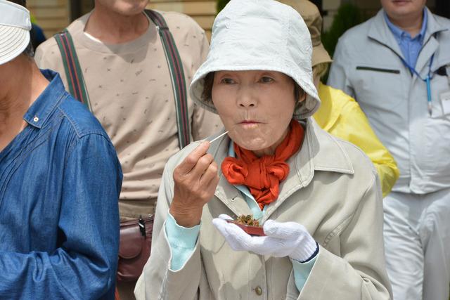 ゴーヤを使った佃煮を爪楊枝で食べている女性の写真