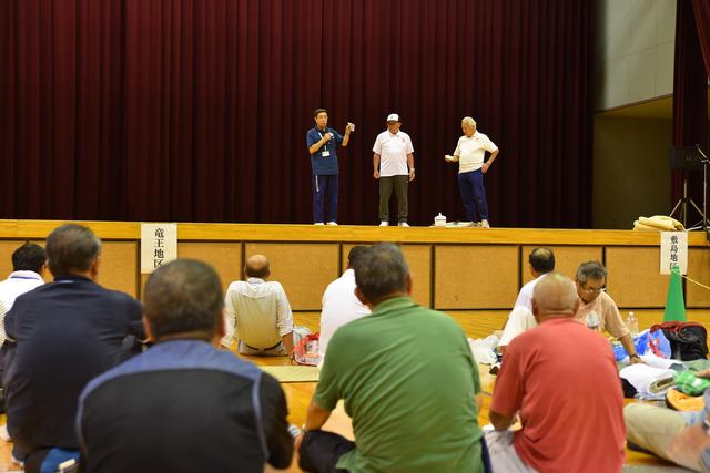 壇上で日赤山梨県支部の3人の男性が参加者を前に、応急手当の指導をしている写真