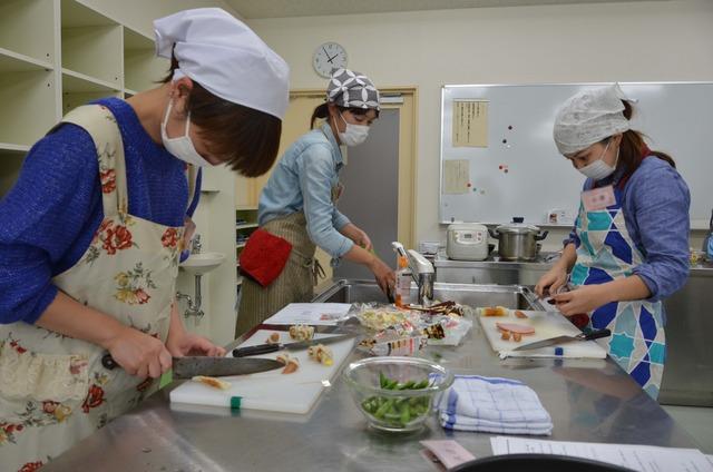 包丁で竹輪を切る2人の女性と野菜を洗う1人の女性の写真