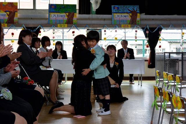 大好きな先生と抱き合う園児と拍手で見守る人々の写真