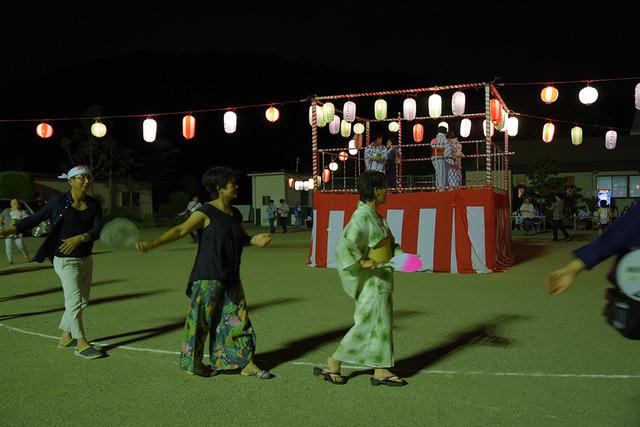 櫓の周りで団扇を持って盆踊りをする人々の写真