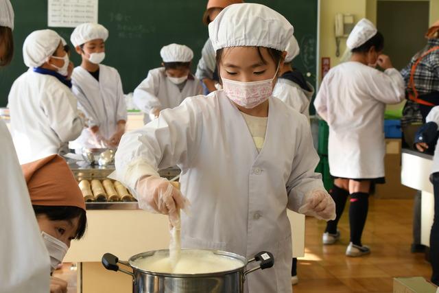 鍋を木べらでかき混ぜている児童の写真