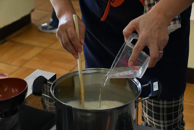 鍋に入れ火にかけた豆乳ににがりを入れている様子の写真