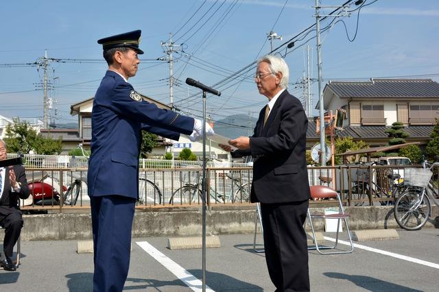 向かい合い、清水韮崎警察署長から米山長塚区長に指定証が手渡される写真
