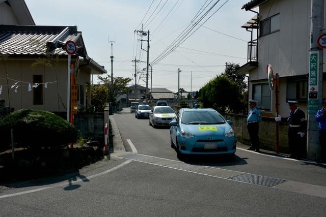 青い車と白い車が警察車両と伴に街中を巡回している写真