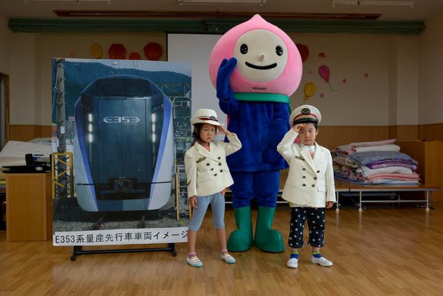 白い駅長の制服を着て敬礼する2人の園児とキャラクターの写真