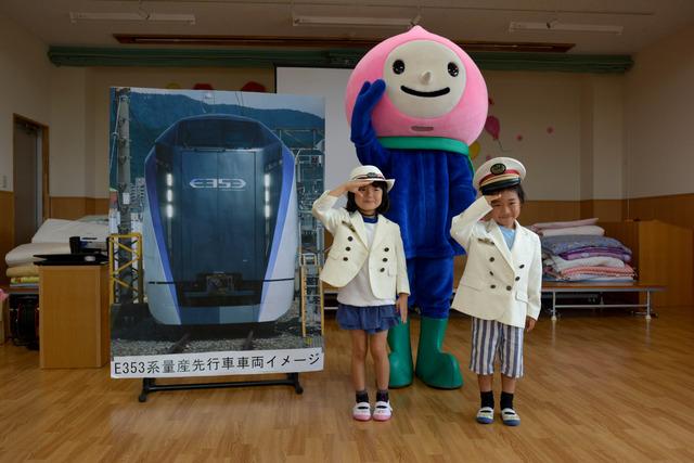 白い駅長の制服を着て敬礼する2人の園児とキャラクターの写真