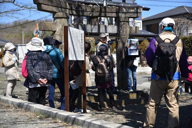 県の文化財である石鳥居の説明を受ける人たちの写真