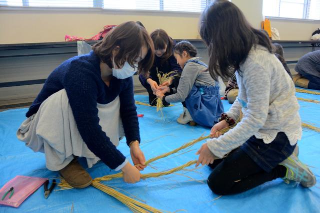 わらをねじりながら編んでいる親子の写真