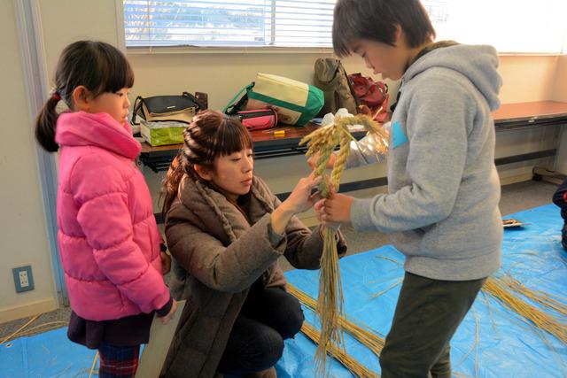 ねじったわらを丸く編んでいる親子3人の写真