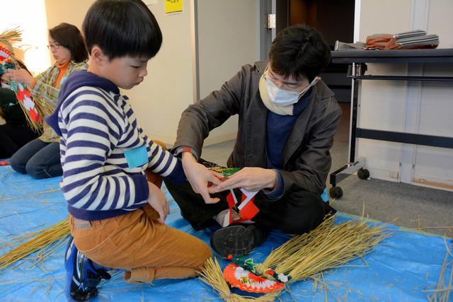 円形のしめ縄に飾りをつける親子の写真