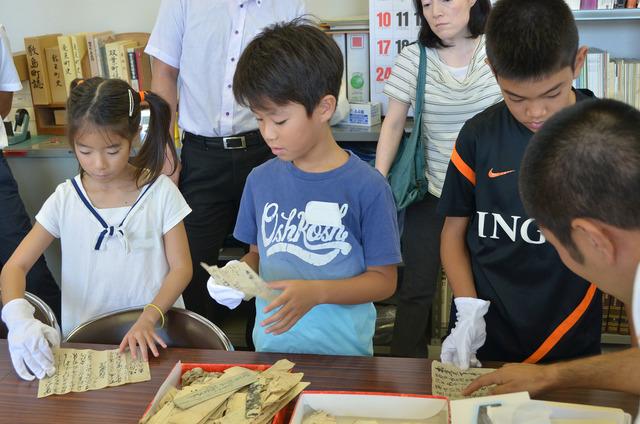 白い手袋をして古文書を手に取り見ている子ども達の写真