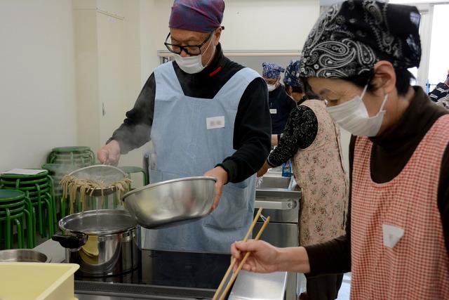 男性が茹で上がった蕎麦を鍋から出している写真