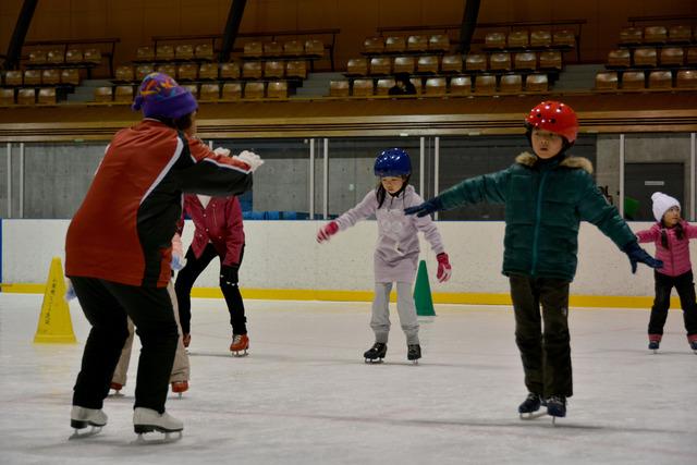 子どもたちがスケートリンクでコーチの指導を受けている様子の写真