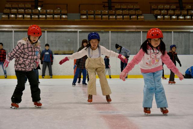 子どもたちが手を広げゆっくりとスケートリンクを滑っている様子の写真